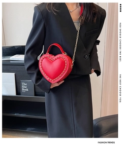Close-up of bright red heart-shaped handbag with glossy finish and gold chain edge