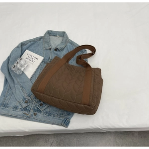 Close-up of brown quilted tote bag with leaf pattern texture and canvas strap