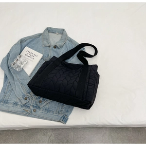 Flat lay detail of a black quilted tote bag displayed over a denim jacket on white fabric