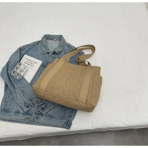 Detail showing khaki quilted tote bag texture and side pocket on blue denim background