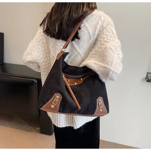 Detail of black corduroy tote bag with brown leather accents and metallic studs