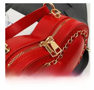 Macro detail of smooth golden zipper and metal chain strap on red heart-shaped handbag