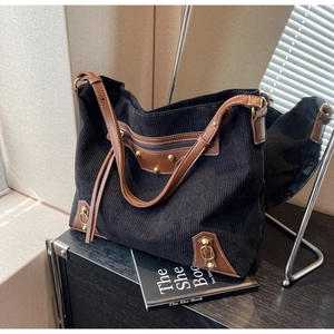 Close-up of black corduroy tote bag featuring brown leather trim and tassel details