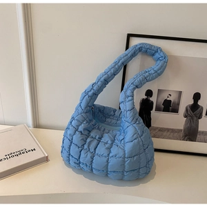 Detail of light blue quilted cloud hobo bag with padded texture on artistic white display