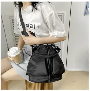 Detail of a black nylon drawstring bucket bag with a wide strap on a model