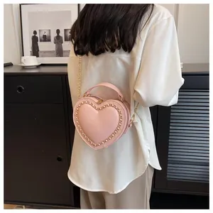 Detail view of pink heart-shaped bag with gold chain strap worn by a model in a room