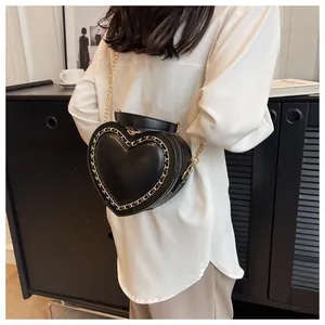 Detail of a black heart-shaped handbag with gold chain trim on a white shirt background