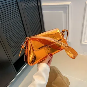 Glossy orange patent leather baguette bag with wide shoulder strap held by hand