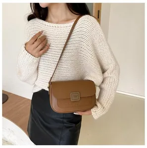 Detail of a brown leather crossbody bag featuring a square buckle and textured suede panel