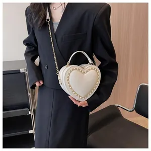 Detail of a heart-shaped crossbody bag in cream leather with gold chain trim and handle