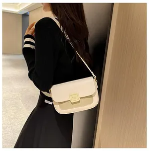 Detail view of a cream leather crossbody square bag with a gold buckle and shoulder strap