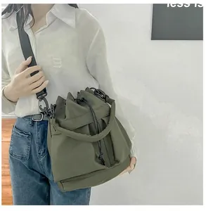 Model wearing an olive green nylon bucket bag with a functional drawstring and black strap