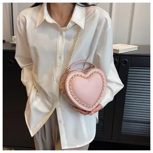 Close-up of pink heart-shaped bag with gold chain strap detail on a white shirt