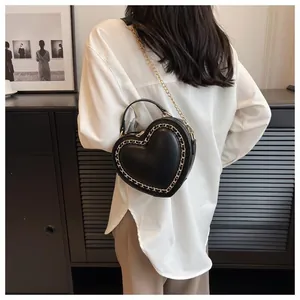 Close-up of black heart-shaped handbag with gold chain trim worn by a model