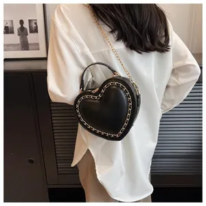 Detail shot of heart-shaped handbag featuring golden chain edges and premium black leather