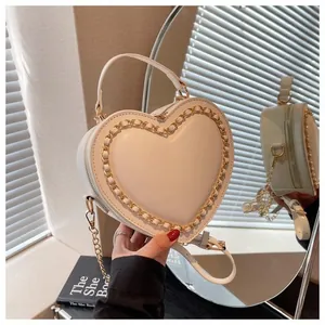 Detail of cream heart-shaped handbag featuring woven chain edges and gold metal strap
