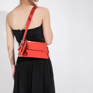 Glossy bright red patent leather baguette bag shown as a shoulder bag on a model