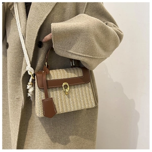 Dettaglio della borsa in paglia intrecciata con finiture in pelle marrone e chiusura oro