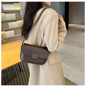 Detail of dark brown leather crossbody bag with flap and metal buckle on beige suit