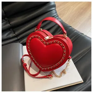 Detail of red heart-shaped matte leather handbag with gold chain on fashion magazine