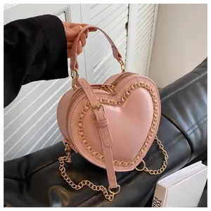 Detail of pink heart-shaped crossbody bag with gold chain trim and double zippers