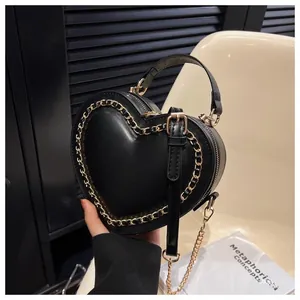 Detail of a black heart-shaped handbag with elegant gold chain trim and leather handle