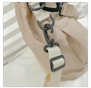 Detail of durable matte black plastic hooks and beige woven shoulder strap on a nylon bag