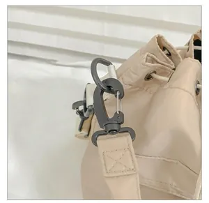 Detailed close-up of dark grey metal snap hook and nylon drawstring on beige bucket bag