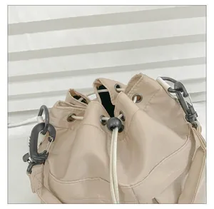 Detail of nylon bucket bag featuring a black carabiner hook and white drawstring closure