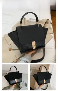 Close-up of black matte winged handbag featuring golden lock and crocodile pattern trim