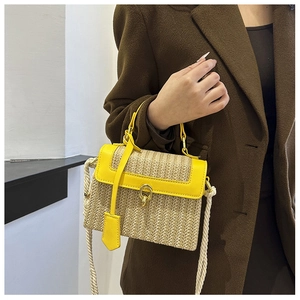 Dettaglio borsa in paglia con finiture in pelle gialla e chiusura dorata su cappotto marrone