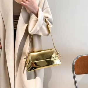 Close-up of a glossy gold mirror-finish baguette bag worn with a white wool coat