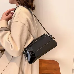 Close-up of a glossy black patent leather baguette bag worn over the shoulder by a model