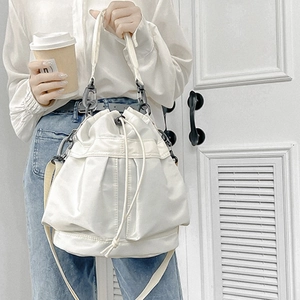White nylon drawstring bucket bag with pleat details shown on model with shoulder strap