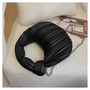 Détail du sac croissant plissé noir avec nœud et chaîne argentée sur fond blanc texturé