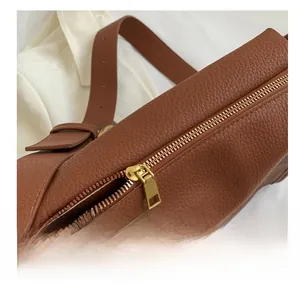 Close-up of smooth gold metal zipper and brown lychee grain leather texture on tote bag