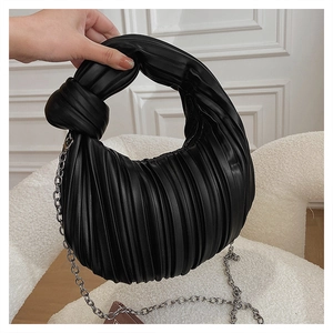 Détail d'un sac plissé noir avec poignée nouée et fine bandoulière en chaîne