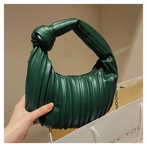 Gros plan d'un sac plissé vert foncé avec poignée nouée et fine chaîne dorée
