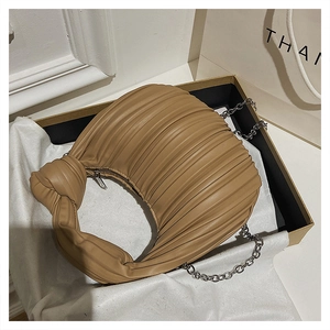 Détail du sac plissé kaki avec poignée nouée et chaîne argentée dans son emballage cadeau