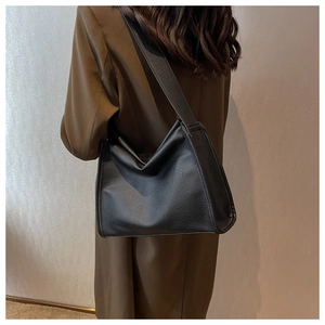 Close-up of black lychee-textured leather hobo bag with wide shoulder strap on a model