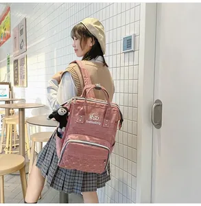 Pink mummy backpack shown in a lifestyle scene with monkey pendant and side pockets