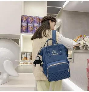 Detail of navy blue denim diaper backpack with a cute plush monkey keychain charm