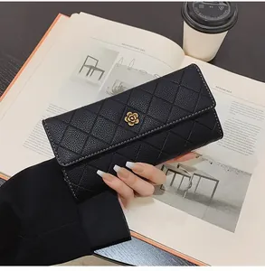 Close-up of black quilted leather wallet with gold camellia logo in a lifestyle setting