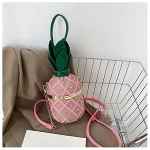 Détail d'un sac seau en forme d'ananas rose avec rivets dorés et bandoulière chaîne