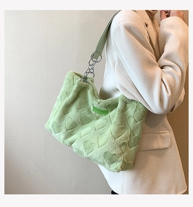 Close-up of light green faux fur tote bag with embossed heart patterns and chain strap