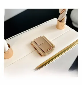 Close-up of golden metal lock and lychee grain leather texture on off-white handbag