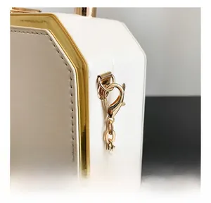 Detailed macro view of golden metal swivel hooks and delicate chain on a white leather bag