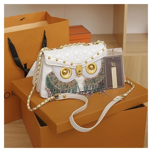 Detailed view of white quilted owl crossbody bag with golden hardware and beaded tassels