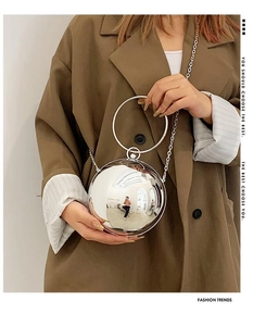 Detail of a silver spherical metal handbag with a round handle and chain strap on a model