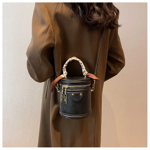 Gros plan du sac seau en cuir grainé noir avec poignée foulard et fermeture dorée